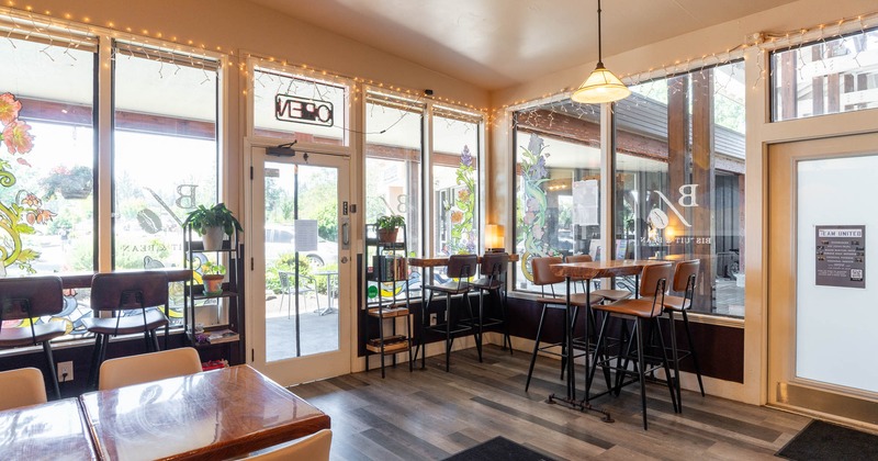 Interior of a café with large windows, bar stools, tables, and natural light