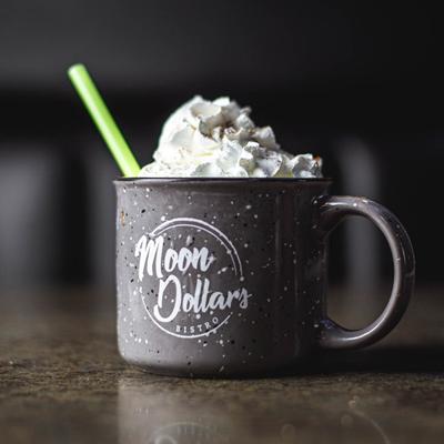 A beverage topped with whipped cream in a mug with the restaurant's logo.