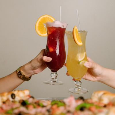 Two people toasting with sangria and sharing a pizza together.