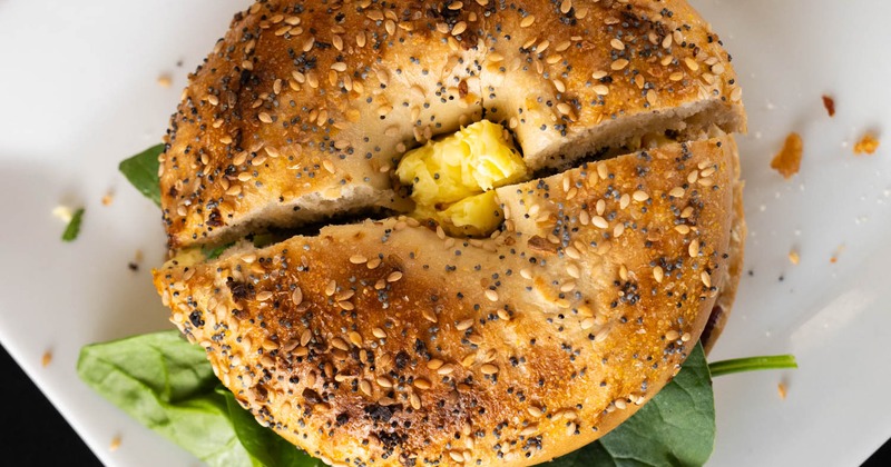 A sesame seed bagel sandwich with scrambled egg and fresh spinach