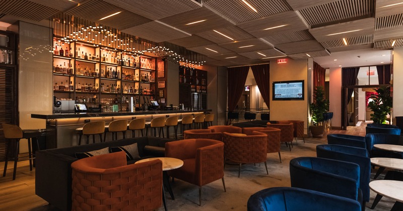 A modern bar with a long countertop, bar stools, cozy seating with armchairs and small tables