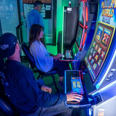 People playing slot machines with colorful screens in a gaming space.