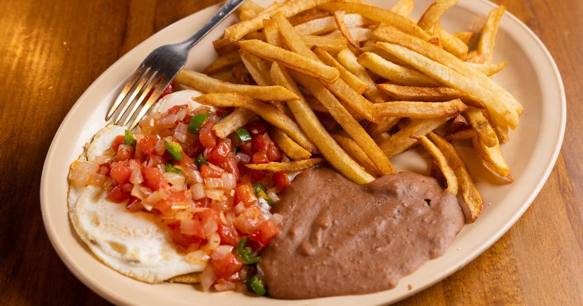 Fried eggs topped with fresh salsa, served alongside refried beans and fries
