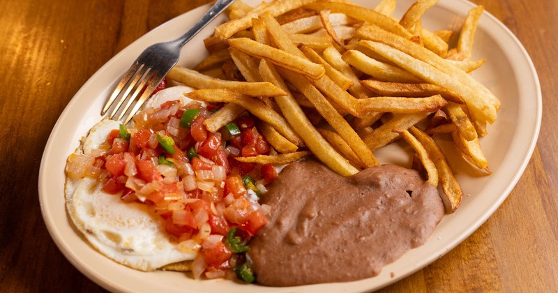 Fried eggs topped with fresh salsa, served alongside refried beans and fries