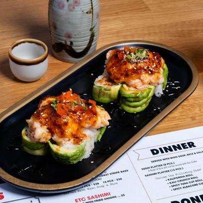 Shark Bait roll on a black platter, a sake set, beer, and menu on a wooden table.