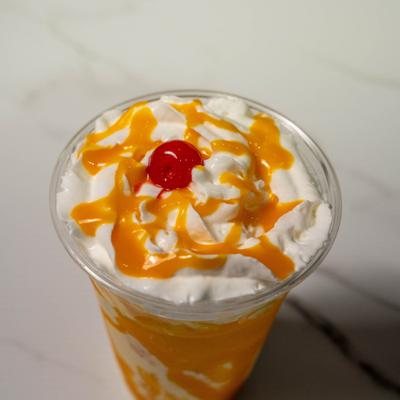 Mango milkshake with whipped cream topping and maraschino cherry garnish.