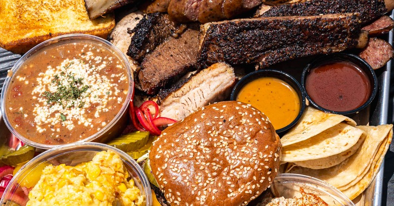 Close-up barbecue feast featuring brisket, ribs, burger, beans, and sauces