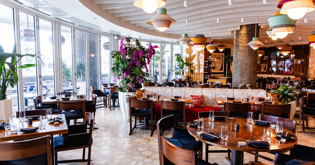 Interior - wooden tables and dark blue chairs, large windows, plants and colorful pendant lights