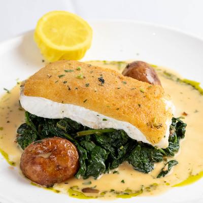 Halibut filet on sauteed spinach with potatoes in creamy sauce and lemon half on a plate.