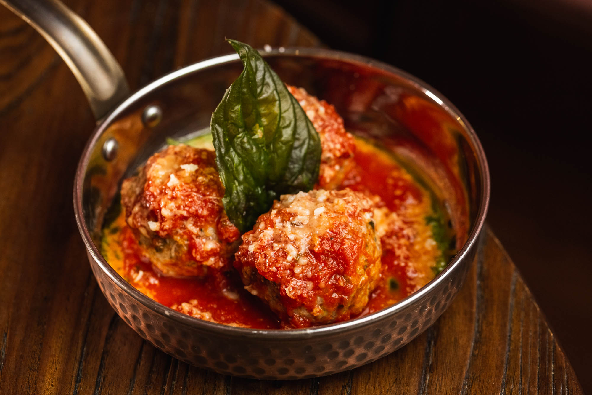 Three meatballs in a tomato sauce, topped with Parmesan and basil