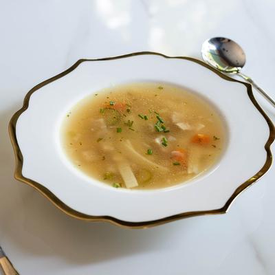 A white plate of chicken noodle soup served on a white table.