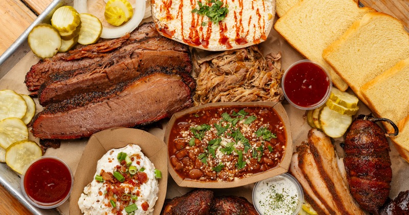 A tray of ribs, pulled pork, and sausage slices, served with drinks