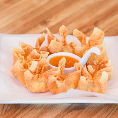 Crab Rangoon served with plum sauce on a white rectangular plate.