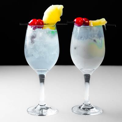 Two cocktails garnished with pineapple and cherries.