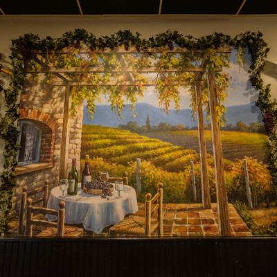 Wall mural of vineyards with table is set with wine bottles in the foreground.