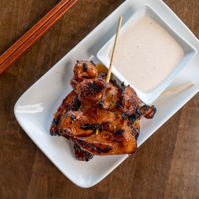 Marinated chicken on a skewer served with a dish holding creamy sauce.