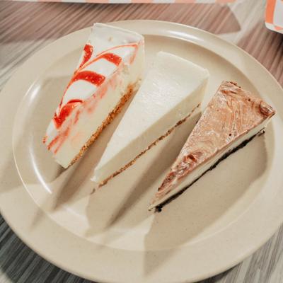Three slices of cheesecake on a plate, strawberry, New York, and chocolate.