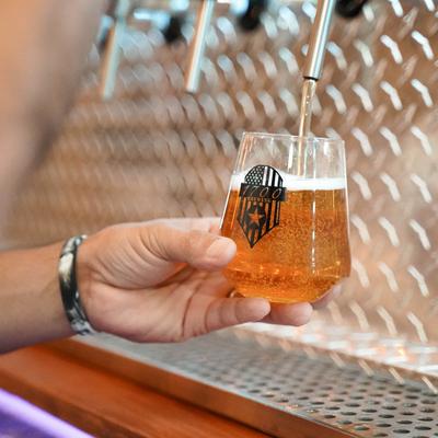 A hand is shown filling a glass with amber beer from a tap.