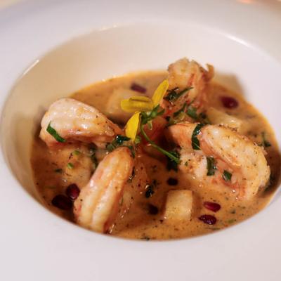 Shrimp in a creamy sauce with herbs and pomegranate seeds, garnished with a yellow flower.