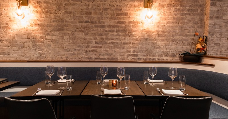 Interior with brick walls, banquette, chairs and tables set with wine glasses