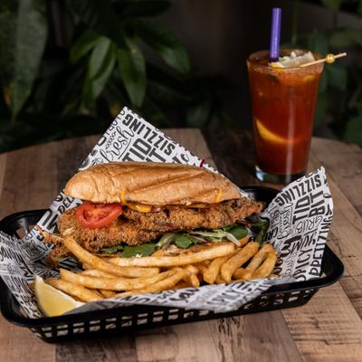 Soft shell crab sandwich with fries and a cocktail in a background.