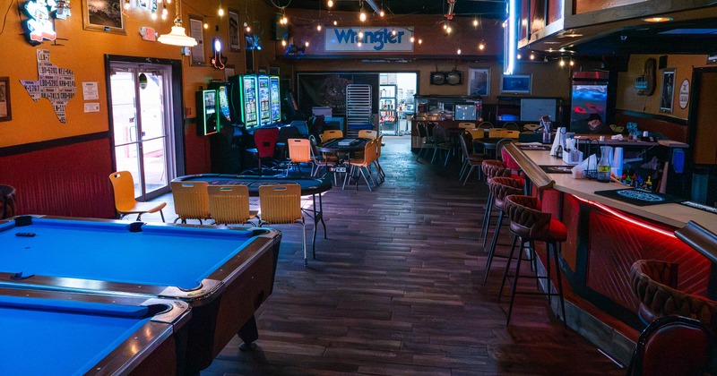 Interior with blue pool tables, arcade machines, tables, bar seating, and colorful neon signs