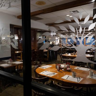 Interior with wooden tables set for guests, seen through glass windows with tree designs.