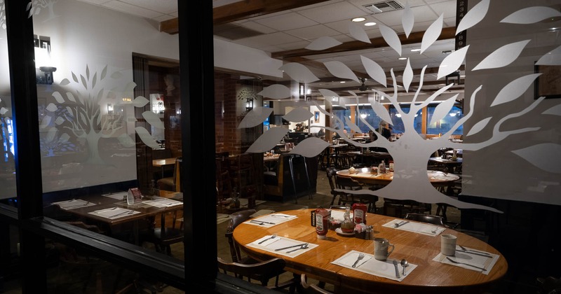 Interior with wooden tables set for guests, seen through glass windows with tree designs