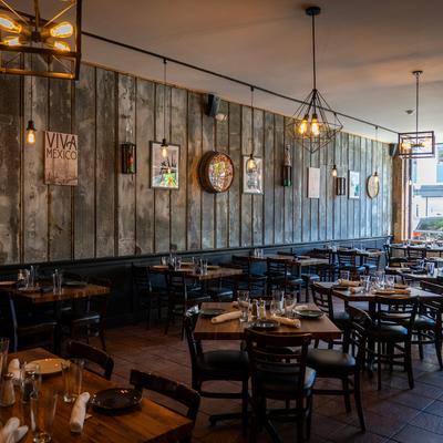 Interior with set dining tables, modern lighting, and artwork on a wood-paneled wall.
