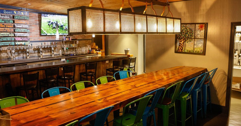 Interior, long wooden top community tables with stools, bar in the back, red brick wall