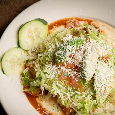 Enchiladas topped with shredded lettuce, tomatoes, avocado, and crumbled cheese.