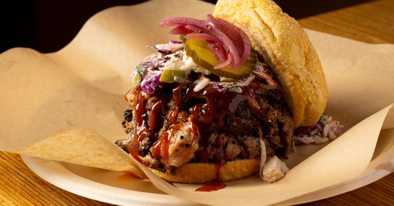 A loaded pulled pork sandwich with coleslaw, pickles, and barbecue sauce
