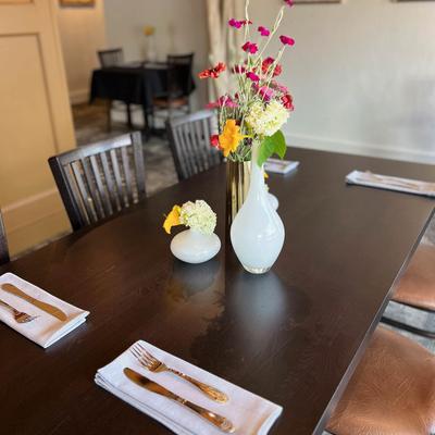 A wooden dining table set with napkins, cutlery, and two vases of flowers.