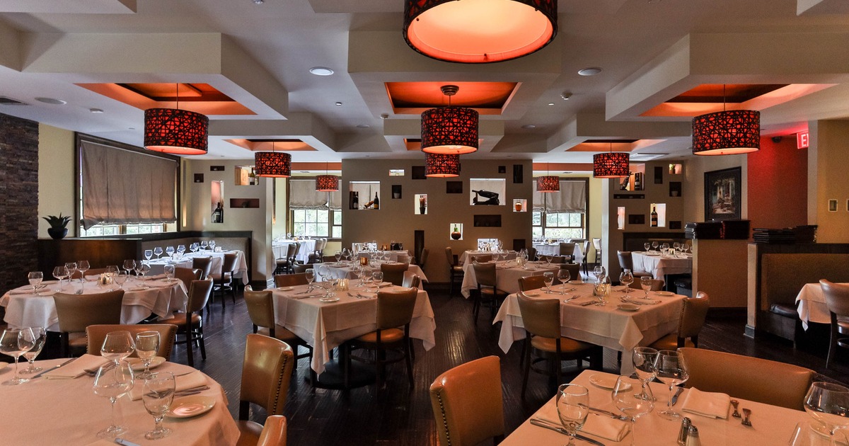 Elegant restaurant interior with red pendant lights, white table settings and tan leather chairs.