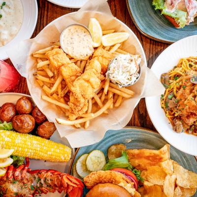 Assorted seafood dishes with fries, lobster, and pasta on a wooden table.