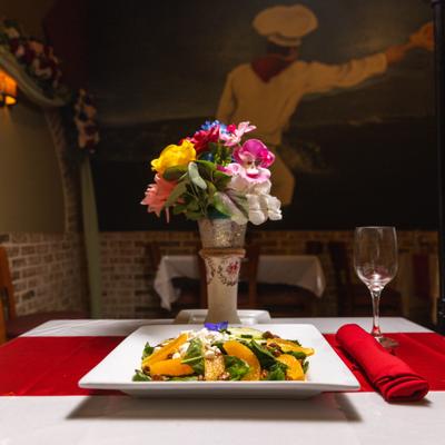 Spinach, orange and feta cheese salad served on a restaurant table with flowers.