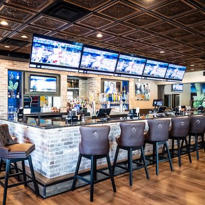 Bar with high-backed stools and multiple screens above the it.