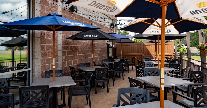 Outdoor patio area featuring grey tables, black chairs, and multiple branded umbrellas