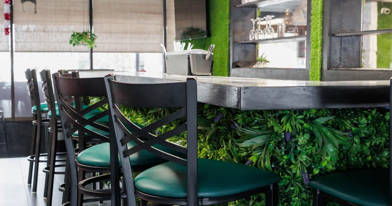 Lush artificial green foliage covering the bar front with high backed bar stools