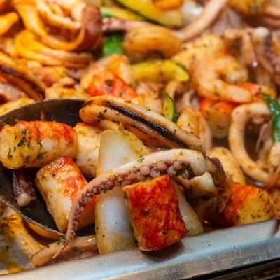 A colorful seafood dish featuring grilled squid tentacles, shrimp, and vegetables in a tray.