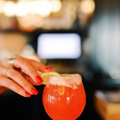 A hand garnishing a bright red cocktail with a lemon wedge.