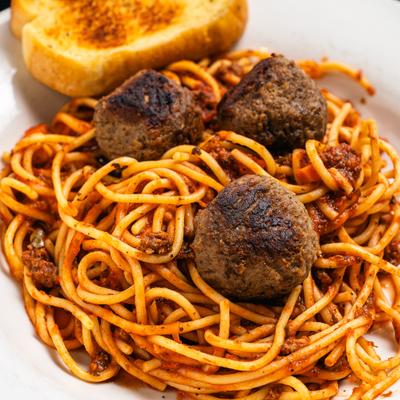 Meatballs served over marinara spaghetti with toasted bread.