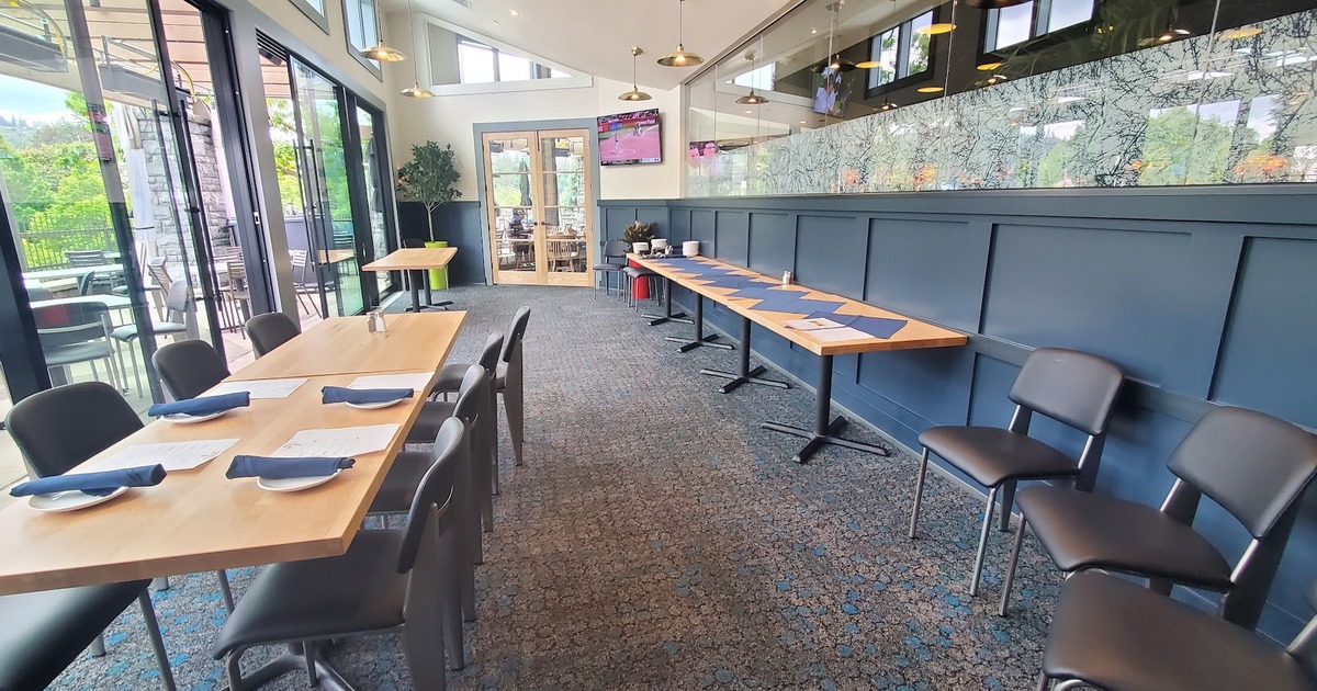 Bright interior with tables, chairs, large windows, and a TV