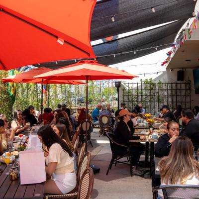 Outdoor restaurant patio with red umbrellas and a crowd of people.
