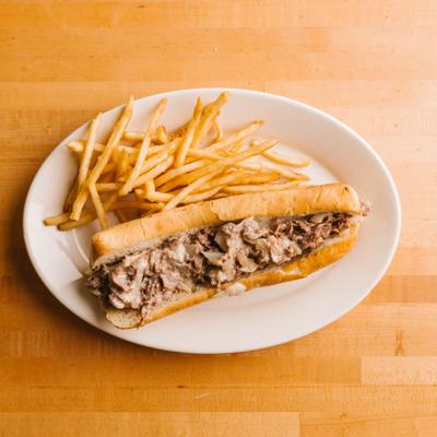 Philly sandwich with fries on a white plate.