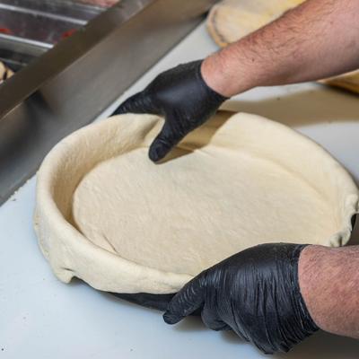 Hands in black gloves shaping pizza dough inside a pan.