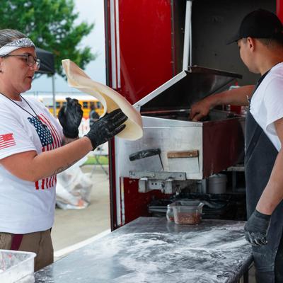 Food truck workers making fresh pizza dough at an outdoor event.