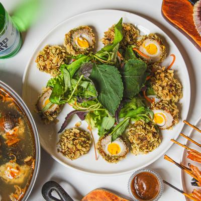 Halved crispy scotch eggs with yellow yolks served over a green salad.