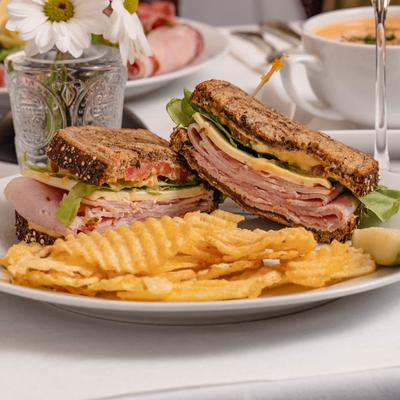 Grilled ham and cheese sandwich, with lettuce, tomato, mayo, and a side of potato chips.