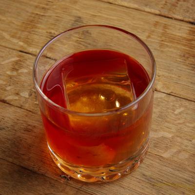 Glass of whiskey with large square ice cube.